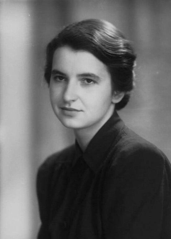 National Portrait Gallery, London. Black-and-white portrait of Rosalind Franklin, wearing a dark collared blouse, her dark hair parted to one side and swept back. She looks towards the camera with a composed expression against a softly blurred background.